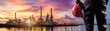 © May Chanikran - Engineer admiring stunning refinery at sunset, wearing safety gear, showcasing industrial progress with vibrant sky backdrop.