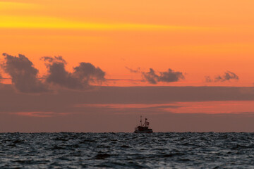 Seascape with smal fisher boat and red sky at dawn.