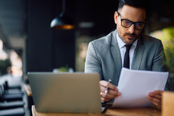 Male entrepreneur going through business reports while working on laptop in café.