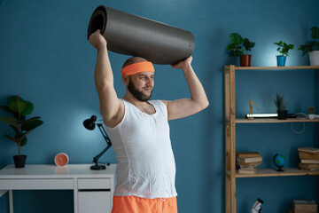 Wall Mural - Man working out with yoga mat at home in stylish workout attire, blue background