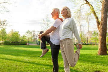 elderly couple of seniors man and woman doing exercises and training in the park outdoors, gray-haired grandparents playing sports and active lifestyle in nature