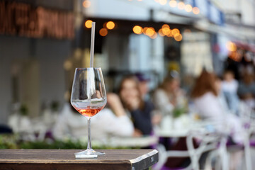 Wine glass with cocktail straw on blurred background of people in street cafe