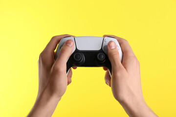 Man using wireless game controller on yellow background, closeup