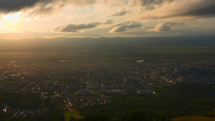 Wall Mural - Top view of city in green valley with sun on horizon. Clip. Beautiful landscape of sunny green valley with town on summer day. Bright sun shines down on valley with town