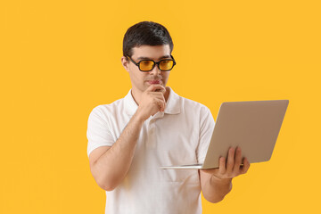 Thoughtful male programmer with laptop on yellow background