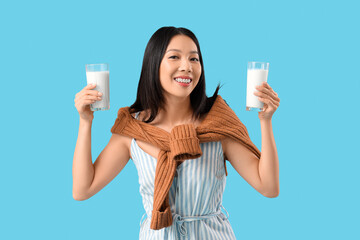 Sticker - Young Asian woman with glasses of milk on blue background