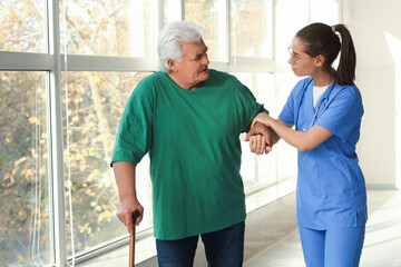 Wall Mural - Nurse helping senior man with stick to walk at hospital