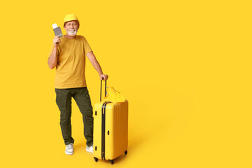 Poster - Mature man with passport and suitcase on yellow background. Travel concept