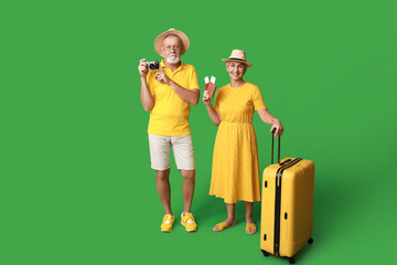 Wall Mural - Mature couple of travelers with passports, photo camera and suitcase on green background