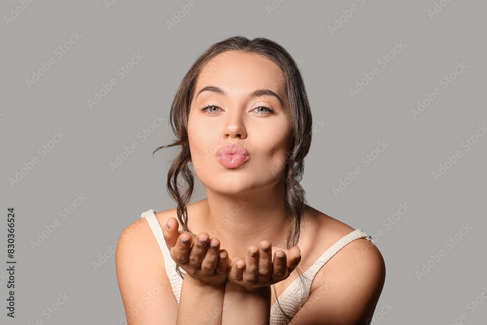 Young woman with beautiful lips blowing kiss on grey background
