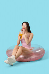 Poster - Beautiful young woman in beachwear with cocktail on swim ring against blue background