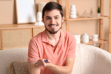 Wall Mural - Diabetic young man using lancet pen on sofa at home