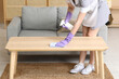 © Pixel-Shot - Female maid cleaning table near sofa in living room
