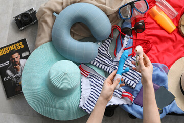 Woman packing vibrators into suitcase with beach accessories and cosmetics on floor, closeup