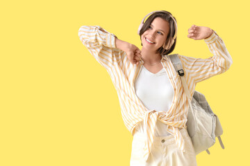 Wall Mural - Happy female student with backpack and headphones dancing on yellow background