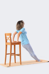 Wall Mural - Sporty mature woman with chair doing yoga on mat against light background