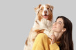 © Pixel-Shot - Young woman with Australian Shepherd dog on light background, closeup