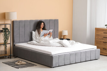 Sticker - Young African-American woman reading magazine on soft mattress at home