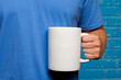 © Moose - A blank white coffee mug held in the style of the arm of an attractive man in front of a blue background
