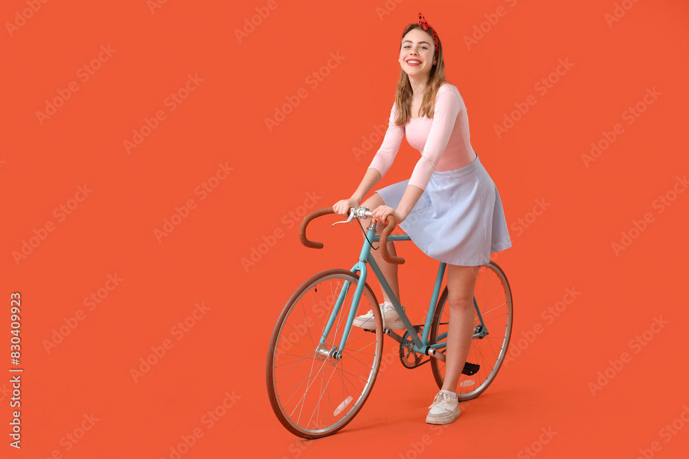 Beautiful young happy woman riding bicycle on orange background