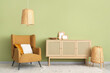 © Pixel-Shot - Brown armchair and wooden cabinet near green wall