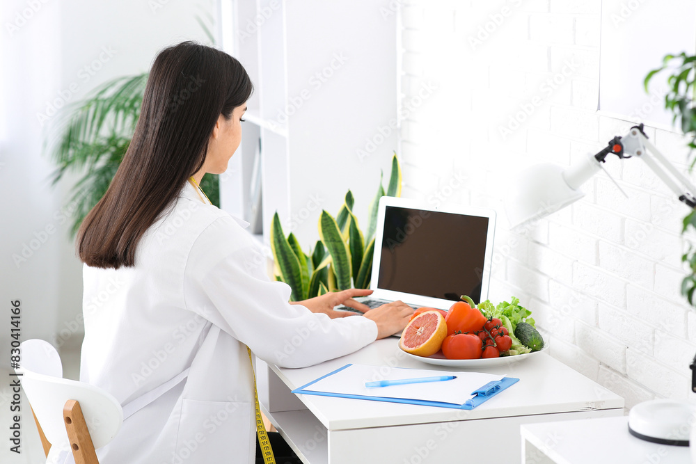 Female nutritionist working with laptop at table in office