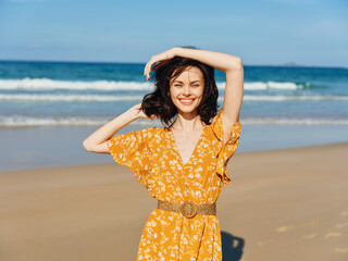 Wall Mural - Woman in yellow dress standing on beach with hands on head, enjoying the beauty of the sea and sky