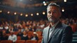 © visoot - Business casual dressed middle-aged handsome man is standing on a stage, looking straight at the camera and posing confidently. In background the crowd of people is watching the show. Generative AI.