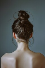 Wall Mural - A woman with a bun on her head. The bun is messy and the hair is brown. The woman's back is showing, and her neck is visible