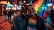 © Watchara - A dark night scene of a city street, where two real gay men of different races, one black and one white, are holding a rainbow flag and smiling. They are looking at the camera with confidence and