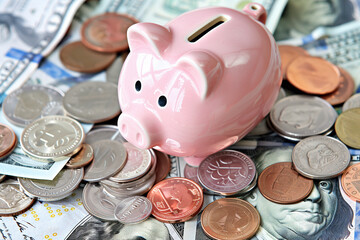 Aufkleber - A piggy bank is sitting on top of a pile of coins and bills. The coins are of various sizes and colors, including silver, gold, and bronze. The bank is pink and has a cute design