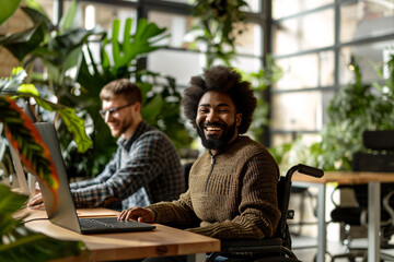 A young african american man with disability smiling and looking in the camera while working on laptop in modern office