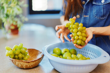 Wall Mural - Woman holding bowl of green grapes in front of another bowl of green grapes, healthy fruit concept