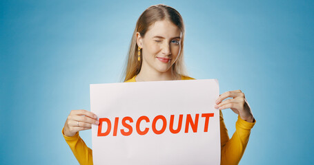 Canvas Print - Woman, wink and discount poster in studio for shopping, retail or sale announcement of store or shop. Young person or seller in portrait with sign, offer and news for makeup deal on blue background