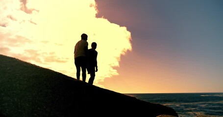 Canvas Print - People, holding hands and fitness in sunset at beach with help on rocks, clouds and outdoor together. Men, support and lift by ocean, sea and silhouette with training, exercise or workout in summer