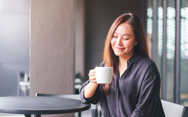 Wall Mural - Portrait image of a beautiful young asian woman holding and drinking hot coffee in cafe