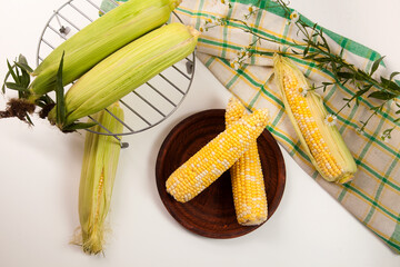 Clay plate with two cobs sweet corn on white wooden background..