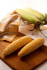 Wall Mural - Cutting board with two cobs sweet corn on white wooden background..