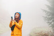 © EdNurg - Lost in the dense fog of the mountains, a worried woman hiker uses her smartphone for navigation, hoping for a strong battery and reliable connection to guide her back.