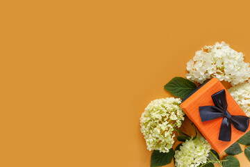 Sticker - Gift box with white hydrangea and rose flowers on orange paper background. Conceptual postcard for  holiday.