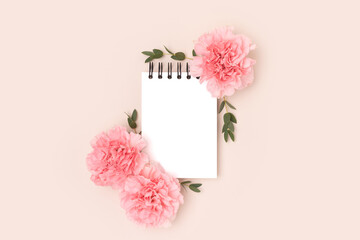 Wall Mural - Empty notepad mockup, pink carnation flowers and green eucalyptus branches on a beige background. Greeting card concept.