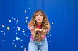 © VISTA by Westend61 - Carefree woman blowing confetti in front of blue wall