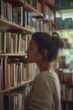 © Jose - Young woman with her hair up checking a bookshelf in a cozy house