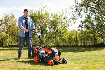 Wall Mural - Man cutting green grass with lawn mower in garden