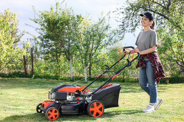 Wall Mural - Smiling woman cutting green grass with lawn mower in garden