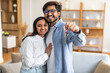 © Prostock-studio - A joyful Indian couple embraces and smiles broadly while holding a set of keys, signifying the purchase of their new home. They stand in a modern, well-lit living room with minimalist decor