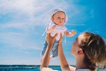 Wall Mural - Mother throwing baby up against the blue sky. Happy family outdoors. Mom and baby at summer on nature. Positive human emotions and feelings.