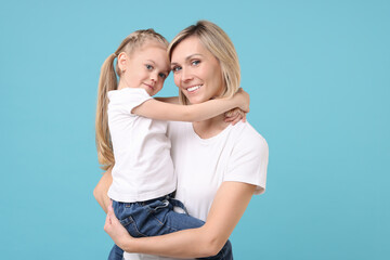 Wall Mural - Family portrait of happy mother and daughter on light blue background