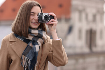 Wall Mural - Beautiful woman in warm scarf taking picture with vintage camera outdoors, space for text