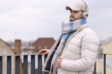 Wall Mural - Handsome man in warm scarf and headphones outdoors. Space for text